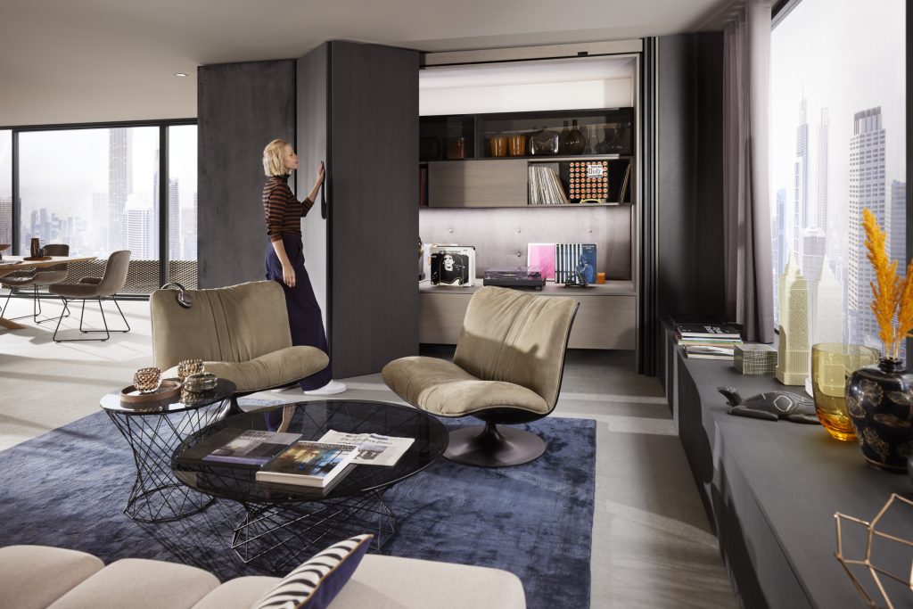 Modern living room where a woman closes a Blum Revego pocket door in the background