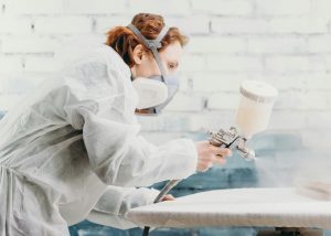 woman spraying paint on a piece of cabinetry using a spray gun